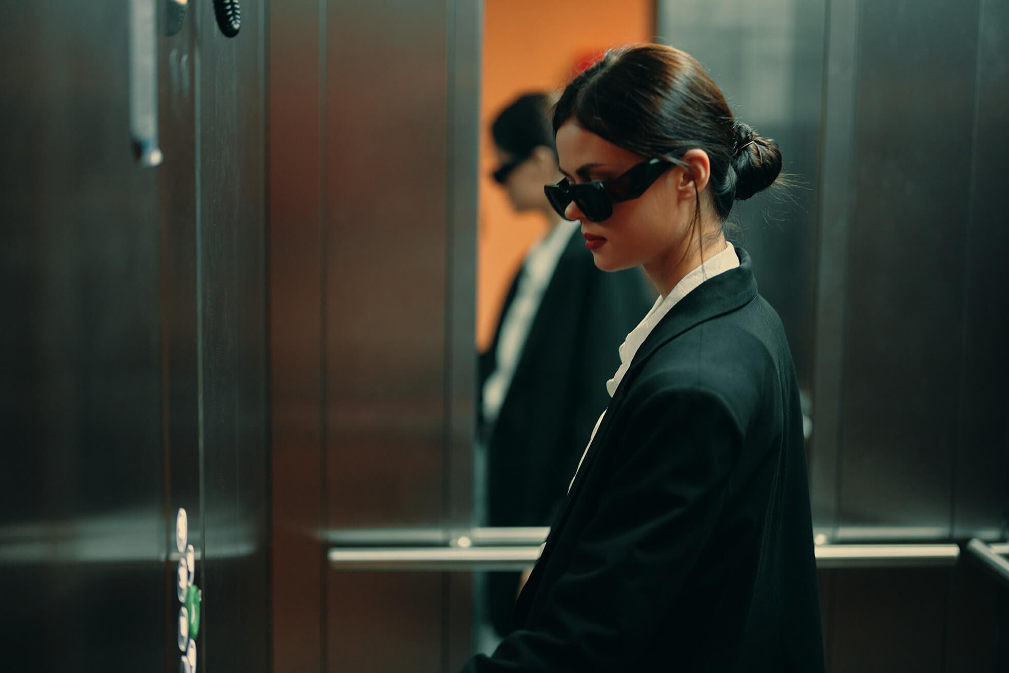 Frau mit schwarzer breiter oversized sonnenbrille steht im fahrstuhl